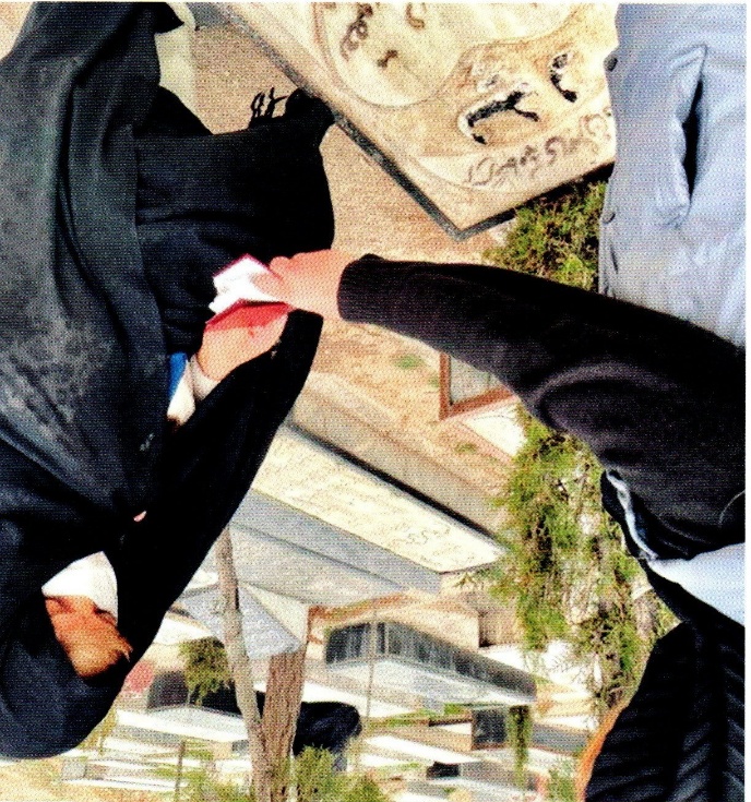 Two people stand among cemetery graves, one holding a sheet of paper.