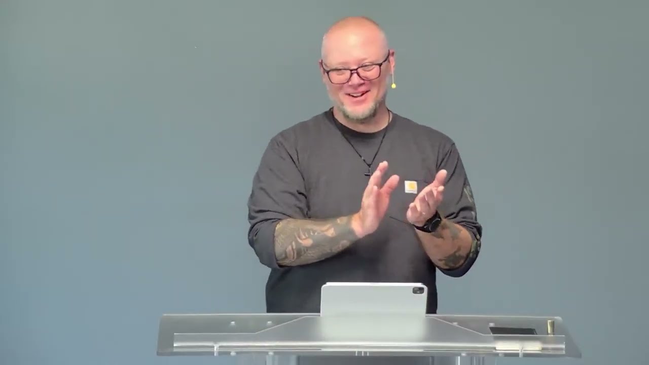 Pastor Ben Nickels smiling and clapping at a lectern during an LCC service.